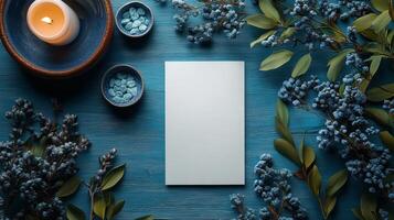 A blank paper with blue flowers and candles on a blue wooden table top view photo