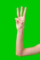 Close Up of a Person's Hand Making the Number Three Gesture Against a Green Screen photo