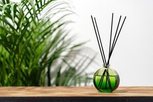 Green Glass Reed Diffuser On Wooden Tabletop With Greenery In Background photo