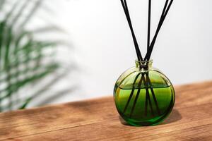 Green Glass Reed Diffuser On Wooden Tabletop With Greenery In Background photo