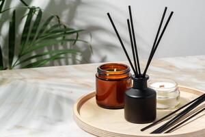 Black Reed Diffuser, Amber Candle, and Wooden Tray on White Surface photo