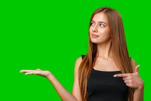 Woman With Long Brown Hair Points To Her Open Palm Against A Green Screen photo