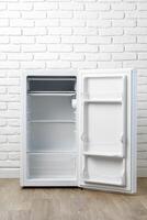 Empty White Refrigerator With Open Door In Front Of White Brick Wall photo