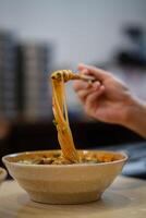 Crop anonymous male with chopsticks eating yummy chinese lanzhou beef noodles and meat in brown bowl at noodle restaurant. photo