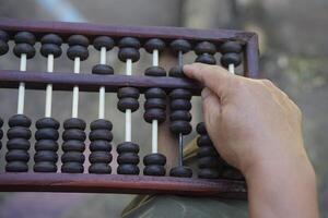 Close up man hand calculate and count wooden abacus. Concept, ancient style calculation. Counting equipment. Calculator. Educational material. Math teaching aid photo