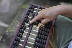 Close up man hand calculate and count wooden abacus. Concept, ancient style calculation. Counting equipment. Calculator. Educational material. Math teaching aid photo