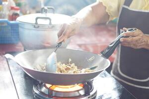 Close up woman is cooking, stirring food in a frying pan on stove by using ladle. Motion shot. Concept, cooking method. Kitchen time. Household daily routine. Preparing breakfast, lunch or dinner. photo