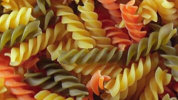 Uncooked Vibrant Colored Fusilli Pasta. A Mesmerizing Culinary Canvas of Multicolored Spirals, Textured Background - Rotating. Turning Colored Dry Pasta. Raw Macaroni - Rotating video