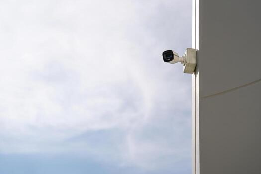 Security camera mounted on wall against cloudy sky photo