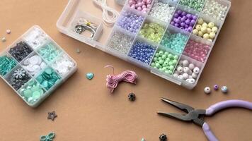 Crafting with colorful beads on a flat workspace with tools and containers in bright daylight video
