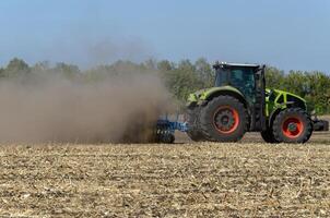 The tractor drives the field. An agricultural tractor on the cultivation of a farm field. Tractor disc harrow plows a farmer's field. Agronomy and the agricultural sector. photo