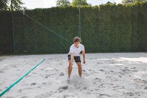 Volleyball player picking up the ball from a sand court, getting ready for the next play in a casual beach volleyball game. Captured in a calm outdoor setting photo