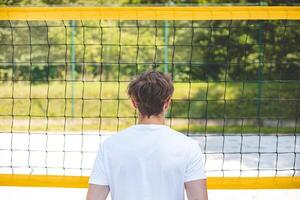 Volleyball player standing face-to-face with the net on a sand court, focused and preparing for the next play. A calm moment captured in an outdoor beach volleyball setting photo