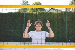 Volleyball player standing face-to-face with the net on a sand court, focused and preparing for the next play. A calm moment captured in an outdoor beach volleyball setting photo