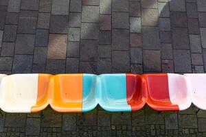 Bright multi-colored plastic seats against a gray sidewalk. photo