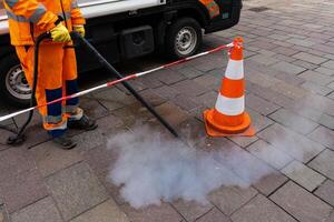 Road worker cleans the pavement with a steam pressure hose. photo