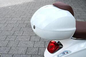 Part of a moped with a white plastic trunk and brake light. photo