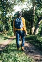 unrecognizable man with backpack and boots holding a camera in front of a path in a forest, nature travel and hiking concept. photo