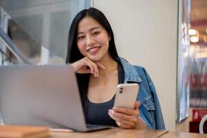 A charming Asian woman working remotely from a coffee shop, sitting at a table with her laptop. photo