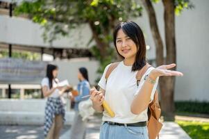 An Asian female college student stands in her college park, smiling at the camera with her palm open photo