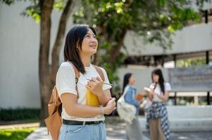 A pretty Asian female college student stands in a college park, looking away as if daydreaming. photo