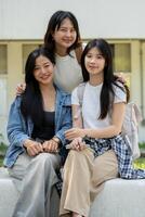 A group of Asian students is sitting on a bench in their college park, smiling at the camera. photo