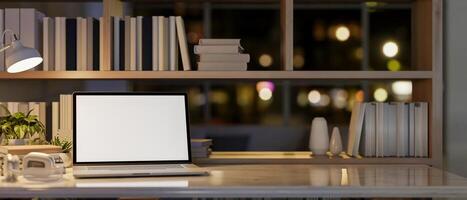 A laptop on a table by a bookshelf in a modern office at night, illuminated by a table lamp. photo