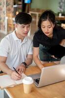 Two focused Asian colleagues are looking at a laptop screen, discussing its content, brainstorming. photo