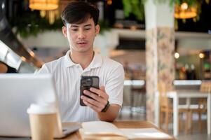 Handsome Asian man is focused on reading chat on his phone while working remotely from a coffee shop photo