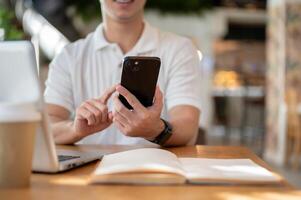 A man is reading chat messages on his smartphone while working remotely from a coffee shop. photo