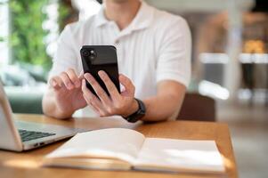 A man is reading chat messages on his smartphone while working remotely from a coffee shop. photo