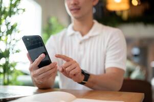 A man is reading chat messages on his smartphone while working remotely from a coffee shop. photo