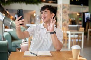 A cheerful Asian man is enjoying a call with his friend on his smartphone in a coffee shop. photo