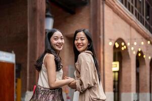Two beautiful Asian female friends enjoy shopping together in the city, smiling at the camera. photo