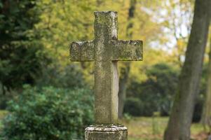 Old stone cross standing in cemetery during autumn photo