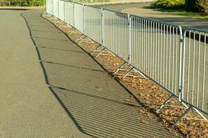 Long metal crowd control barriers casting shadows on asphalt road photo