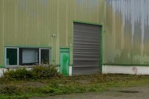 Green industrial building with closed roller shutter door and overgrown grass photo