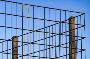 Metal wire mesh fence creating grid pattern against blue sky photo