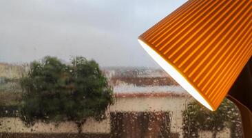 Close-up of rain-streaked window with orange lamp lighting the foreground photo