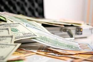 A close-up shot of several US dollar bills spread out on a white surface near a silver case. The bills are in various denominations and some are out of focus photo