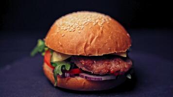 Great Burger with beef cutlet, tomatoes, mushrooms and cucumbers with melted cheese rotates on a wooden Board on a dark background. video