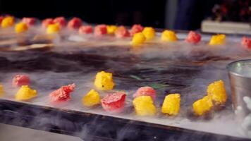 Cold dessert food with dry ice smoke on the background of black ice cream with fruit. Yellow and red pieces of dessert on ice-cream in white steam from liquid nitrogen. video