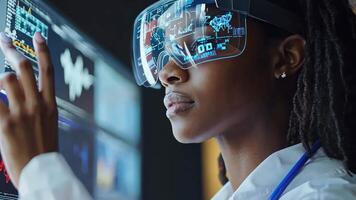 A woman wearing a lab coat and glasses is looking at a computer screen video
