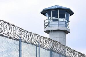 watchtower stands guard over a secure prison surrounded by barbed wire fencing against the sky. photo