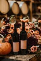 Two bottles of wine sit amongst autumnal flowers and a pumpkin. photo