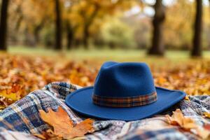 A wide brimmed hat rests on a cozy blanket surrounded by vibrant fall foliage photo