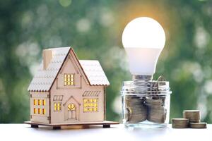 Model house and light bulb with stack of coins money in glass bottle on natural green background,Saving money and energy saving concept photo
