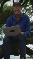 A Man Diligently Working on a Laptop While Seated in a Tree Merging Nature and Productivity video