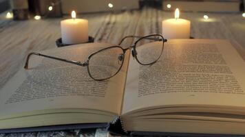 An inviting reading setup features an open book resting on a wooden surface, with a pair of glasses placed on top. Soft candlelight creates a warm ambiance perfect for enjoying literature. video