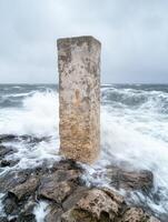 Weathered concrete pillar standing tall against crashing waves photo
